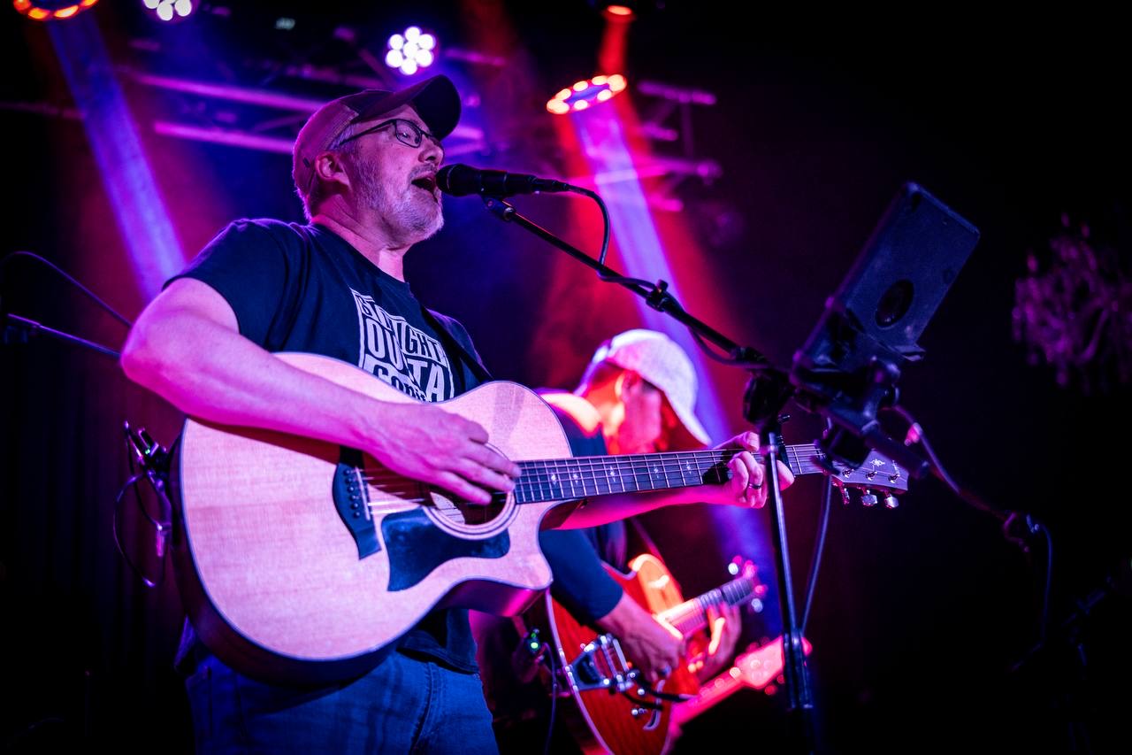 Photo: Noah Martin Photography Lance singing with acoustic guitar under stage lights